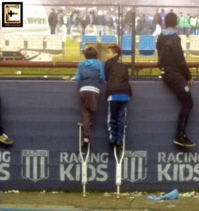 Δύο παιδιά πάνω σε πατερίτσες, βλέπουν αγώνα ποδοσφαίρου.