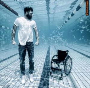 Παραπληγικός, άτομο με κινητική αναπηρία, αιωρείται όρθιος πάνω από το αναπηρικό του καρότσι μέσα σε πισίνα